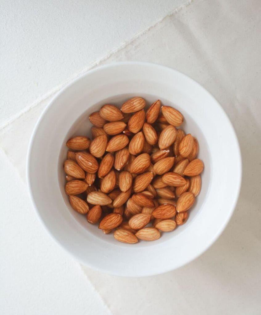 Fresh raw almonds in wooden bowl showing natural brown skin and oval shape
