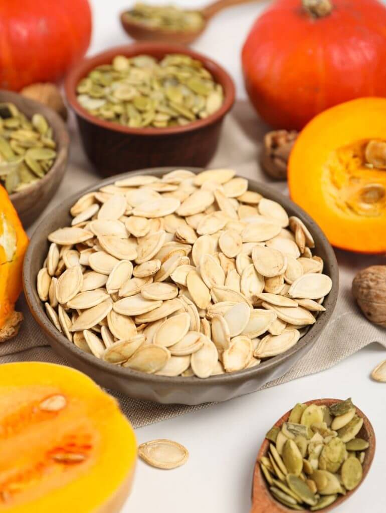 Raw hulled pumpkin seeds scattered on wooden surface showing their flat oval shape and green-white color